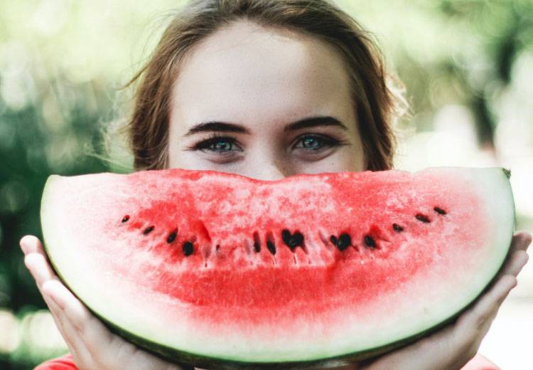 Jugendliche mit einem Stück Wassermelone vor dem Mund - dargestellt als großer lachender Bund