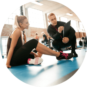 Mann im Trainingsanzug und Trainingsplan im Fitnessstudio erklärt einer Frau in Sportsachen den Trainingsplan