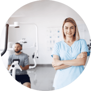 Frau in medizinischer Arbeitskleidung steht in einem Therapieraum, im Hintergrund trainiert ein Mann an einem Sportgerät