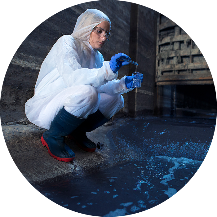 Wissenschaftlerin im weißen Schutzanzug und Gummihandschuhen entnimmt eine Probe aus einem Gewässer
